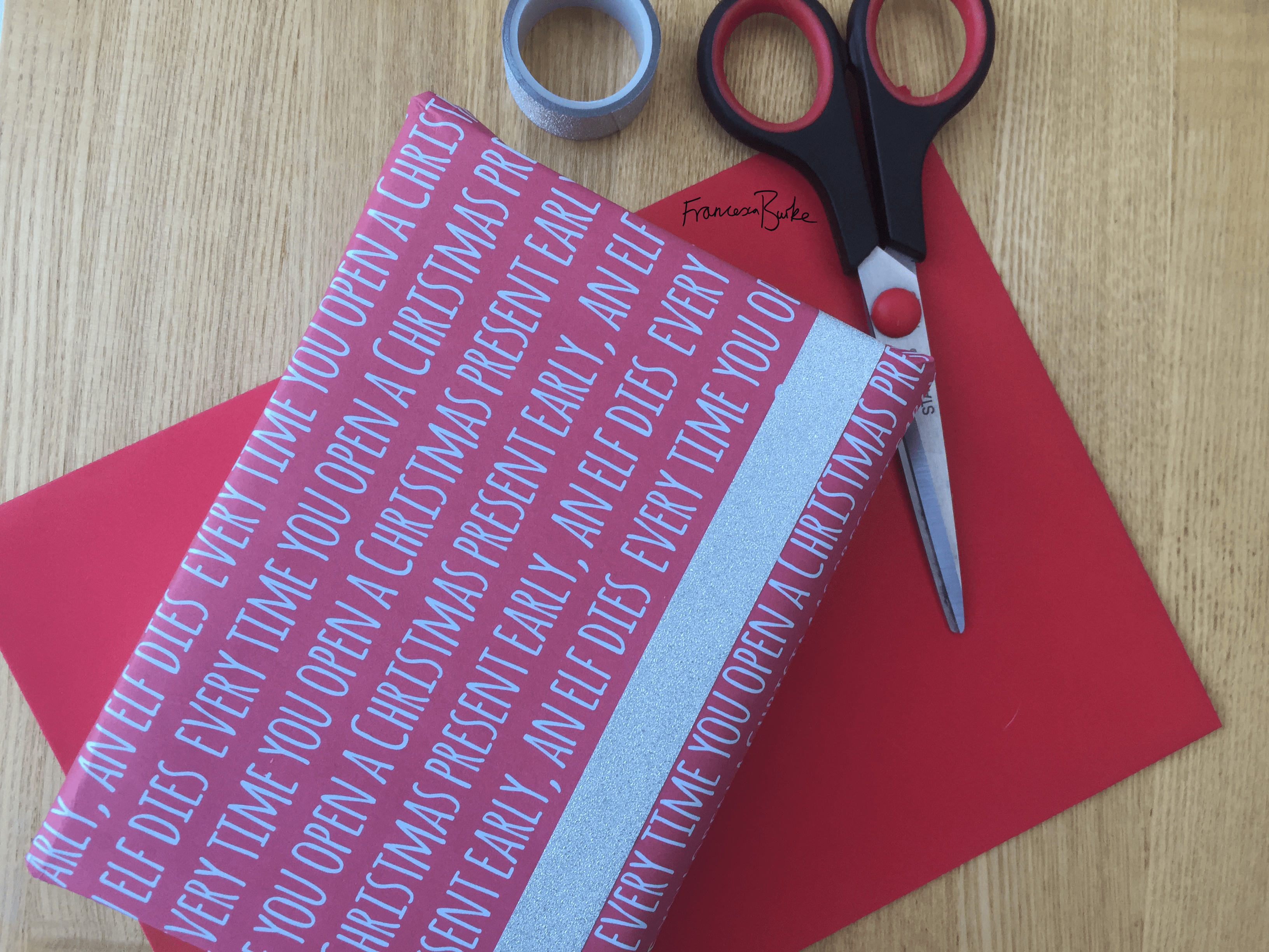 red Christmas wrap reading Every Time You Open a Christmas Present Early, an Elf Dies, next to tape and scissors
