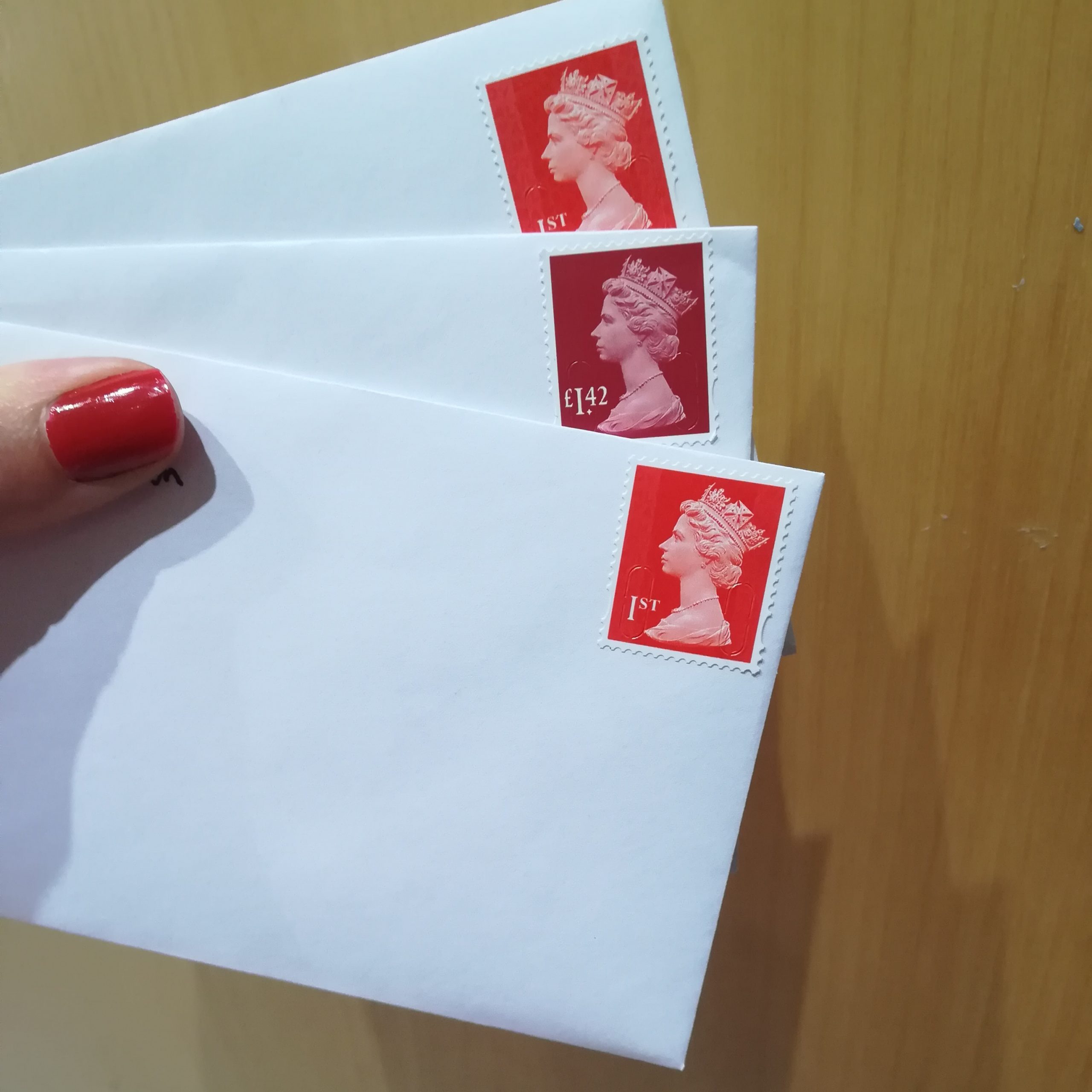 three white envelopes with red stamps, held by a hand with red nail varnish