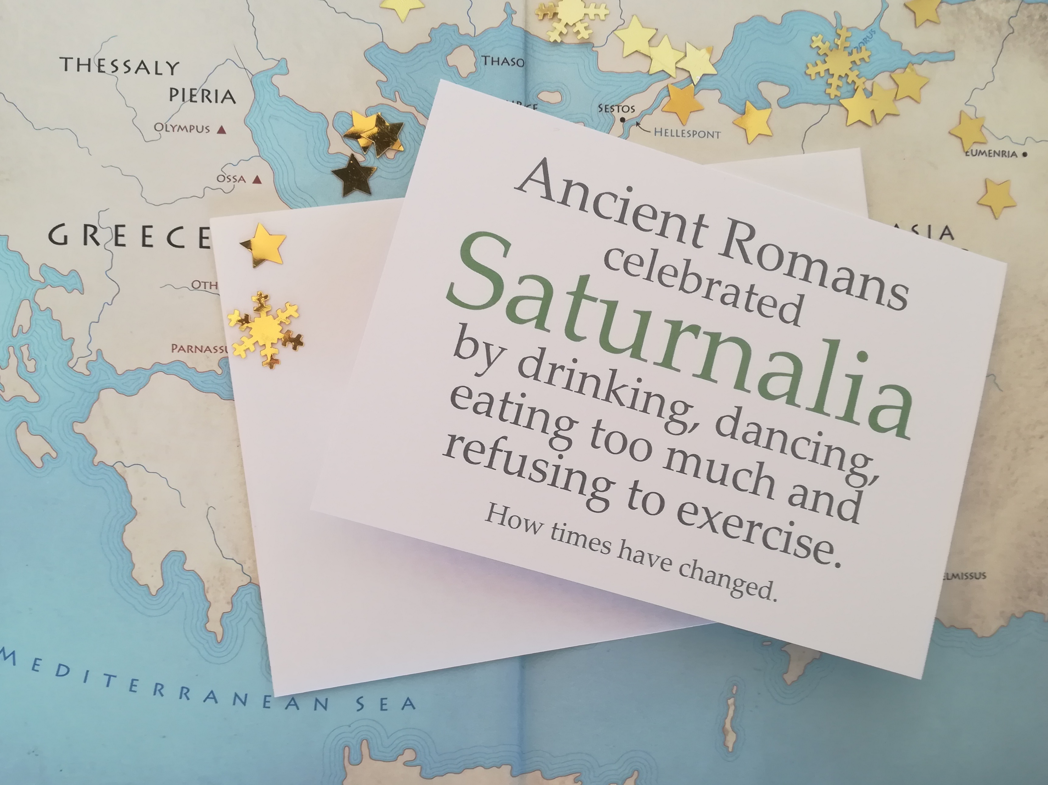 Card on map background reading 'Ancient Romans celebrated Saturnalia by drinking, dancing, eating too much and refusing to exercise. How times have changed.'